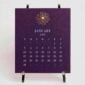 The Printery 2027 Calendar - Aubergine on the chrome easel, white text with starburst engraved in gold | Kneen & Co