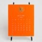 The Printery 2027 Calendar - Orange, white text with starburst engraved in gold | Kneen & Co
